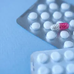 Dwa blistry z białymi tabletkami i jedna kapsułka z różowymi granulkami.