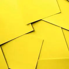 Stos żółtych kartek papieru ułożonych na sobie, tworzących abstrakcyjny wzór.