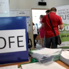 Folder z napisem OFE, ludzie stojący przed banerem ZUS. Czy można wypłacić pieniądze z OFE?