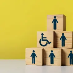 Drewniane klocki tworzą piramidę. Na jednym z nich widnieje symbol niepełnosprawności, obok inne figury ludzi.