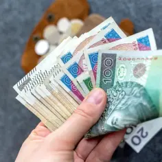 Dłoń trzymająca wachlarz polskich banknotów i monet.