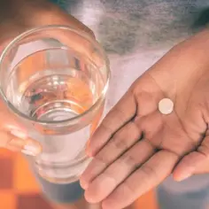 Dłoń trzyma szklankę wody i tabletkę Tylenol.