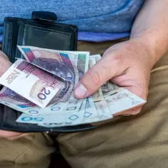 Dłonie trzymające portfel z polskimi banknotami.