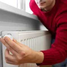 Mężczyzna reguluje termostat grzejnika, oszczędzając energię. PFRON dofinansowanie do ogrzewania może pomóc w pokryciu kosztów.