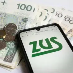 Telefon z logo ZUS na ekranie, obok polskie banknoty i monety.