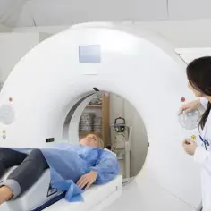 Pacjentka leży na stole tomografu, przygotowana do badania angio-tk tętnic wieńcowych. Lekarka obsługuje aparat.