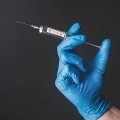 Dłoń w niebieskiej rękawiczce trzyma strzykawkę z napisem "VACCINE".