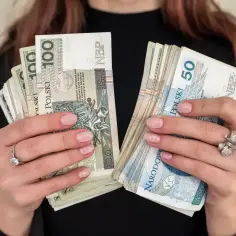 Dłonie trzymające pliki banknotów 100 i 50 zł. Pieniądze mogą być przeznaczone na świadczenie pielęgnacyjne dla kogoś bliskiego.