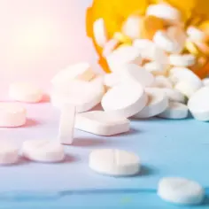 Białe tabletki, w tym leki opioidowe, rozsypane z pomarańczowego pojemnika na niebieskim tle.