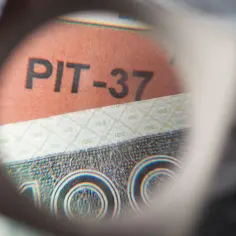 Pod lupą widać napis PIT-37 na tle banknotu 100 zł.