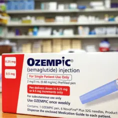 Pudełko leku na cukrzycę Ozempic z wstrzykiwaczem. W tle apteczne półki z lekami.