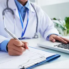 Lekarz w białym kitlu pisze na dokumentach i korzysta z laptopa. Czy do psychologa potrzebne jest skierowanie?