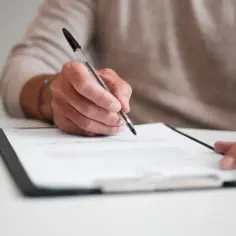 Dłoń pisząca długopisem na dokumencie na białym stole.