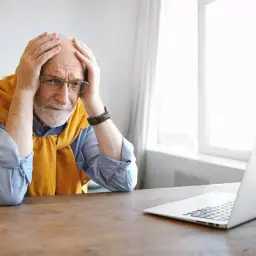Starszy mężczyzna z rękami na głowie, patrzący na laptopa, wygląda na całkowicie niezdolnego do pracy przywileje.