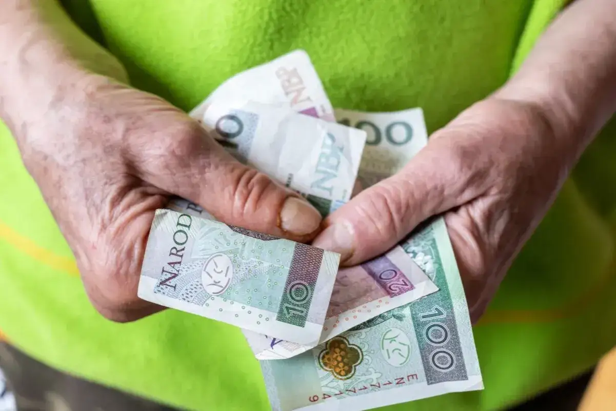 Dłonie trzymają polskie banknoty: 10, 20 i 100 zł. Pytanie o 2 grupę inwalidzką ile pieniędzy.