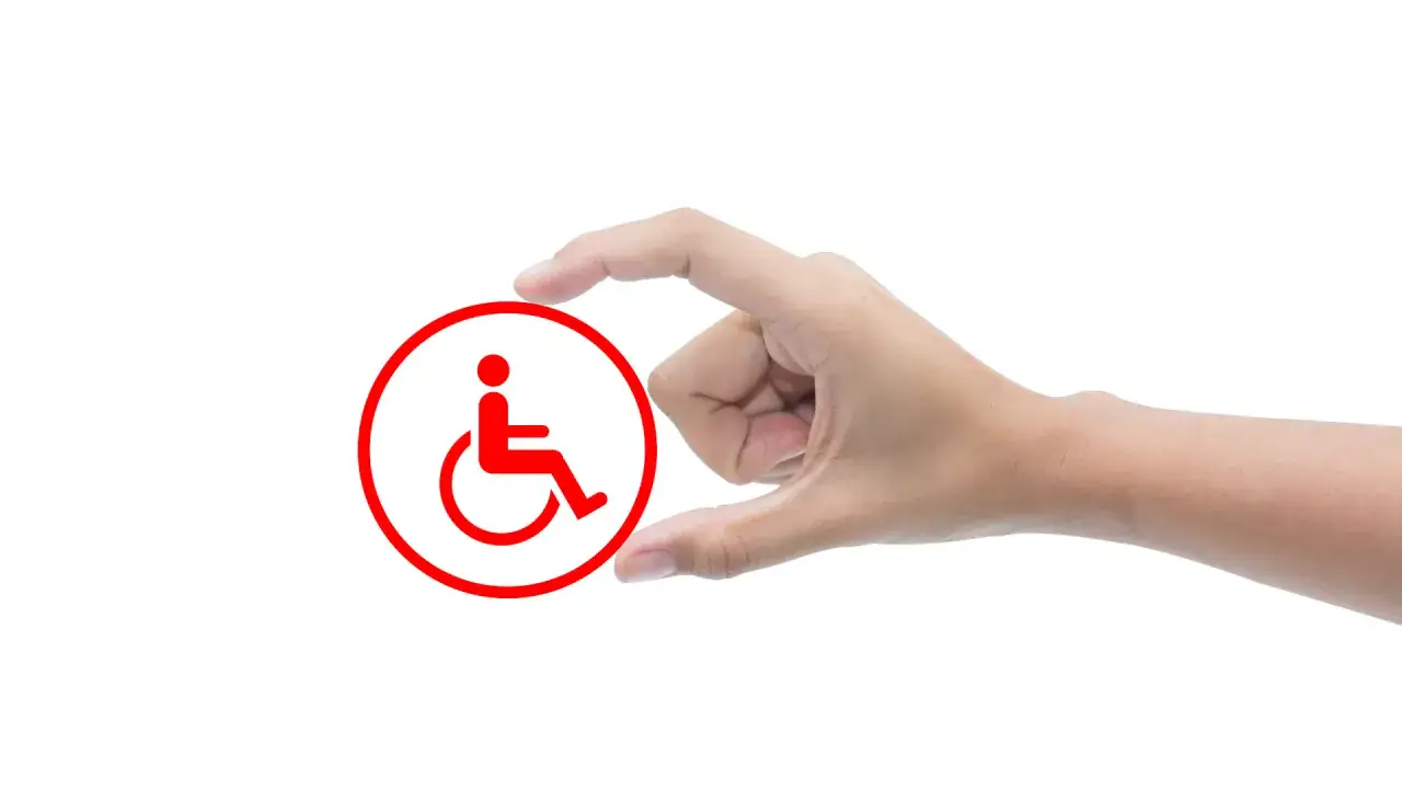 Dłoń trzyma symbol niepełnosprawności. Czerwony okrąg z postacią na wózku inwalidzkim.