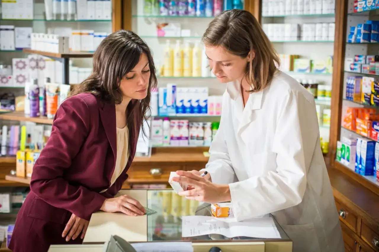 Farmaceutka w białym kitlu pokazuje klientce lek OTC.