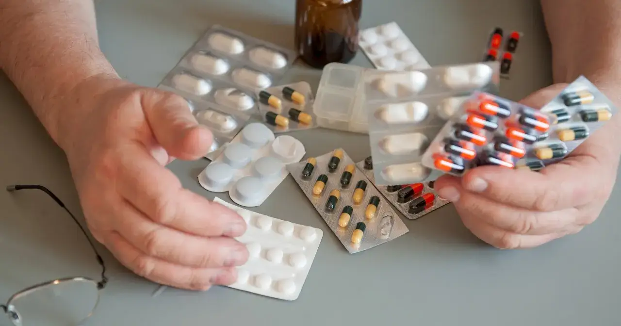 Ręce seniora trzymają opakowania z lekami. Wiele tabletek i kapsułek, być może darmowe leki dla seniorów.
