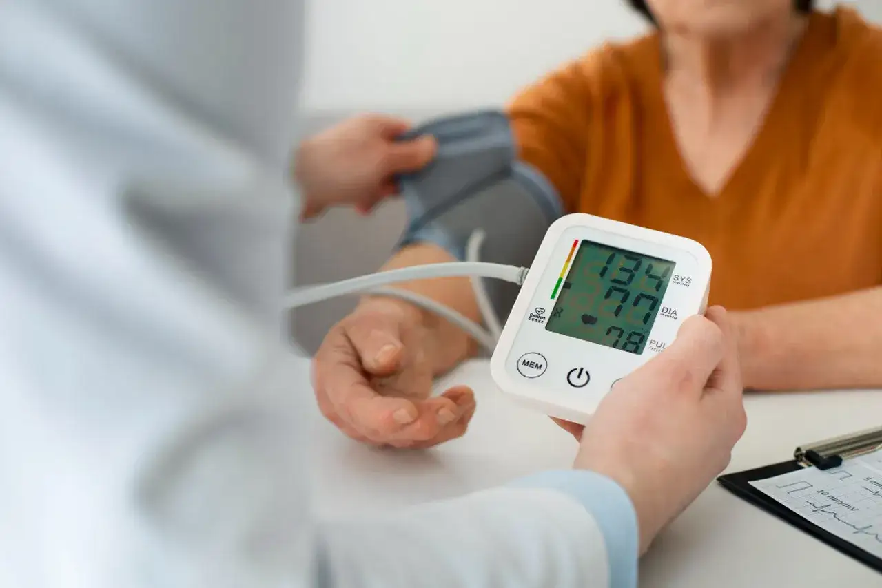 Lekarz mierzy ciśnienie krwi pacjentowi. Na ekranie ciśnieniomierza widoczne są wyniki: 134/77 mmHg.